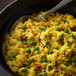 A spoon in a bowl of rice and peas with yellow peppers.