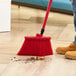 A person using a Lavex red broom to sweep a wooden floor.