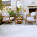 An Outdoor Interiors Eucalyptus patio set with white cushions on a wooden table next to a white chair and potted plant.