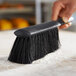 A hand using a black Lavex counter brush to clean up flour on a counter.