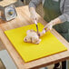 A woman using a knife to cut a chicken on a yellow polyethylene cutting board.