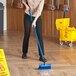 A person scrubbing a floor with a yellow Lavex Flo-Thru scrub brush.