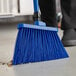 A blue Lavex broom head with a handle sweeping the floor.