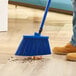 A person sweeping the floor with a Lavex blue broom.