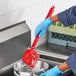 A person in blue gloves using a red Lavex utility scrub brush to wash a pot.