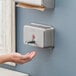 A hand using a Lavex stainless steel horizontal liquid soap dispenser.