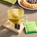 A glass of Stash green tea with a tea bag in it on a table with a pastry.