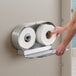 A man's hand reaching for toilet paper in a Lavex stainless steel double-roll toilet paper dispenser.