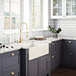 A white Ruvati farmhouse sink in a kitchen with dark cabinets and white countertops.