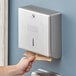 A hand using a Lavex stainless steel paper towel dispenser on a wall.