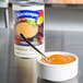 A bowl of Chincoteague Lobster Bisque with a spoon in it next to a can of lobster soup.