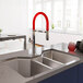 A Ruvati stainless steel triple-bowl sink in a modern kitchen with a red faucet.