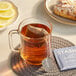 A glass mug of Stash Earl Grey tea with a Stash Earl Grey tea bag on a coaster next to a plate of lemon slices.