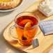 A glass mug of Stash Decaf Earl Grey tea with a Stash tea bag on a wooden tray.