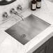 A Ruvati stainless steel rectangular undermount bathroom sink with a faucet over a marble counter.