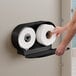 A hand reaching for a roll of Lavex stainless steel toilet paper.