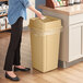 A woman standing next to a Lavex beige square plastic trash can with a lid.