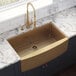 A Ruvati Terraza stainless steel farmhouse sink with a brass and gold finish on a countertop.