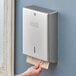 A man with a beard putting a paper towel in a Lavex stainless steel paper towel dispenser on a wall.