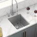 A stainless steel Ruvati undermount sink with wine glasses and a knife on a metal rack.
