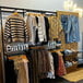 A Udizine black wall-mount retail clothing display with faceouts and shelves holding clothes.
