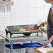 A light-duty electric countertop griddle being used to cook eggs and bacon in a commercial kitchen setting.