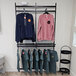 A black UDIZINE wall-mounted retail clothing rack with faceouts and a hanging rail with shelves holding shirts and sweatshirts.