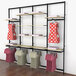 A Udizine black wall-mount retail clothing display rack with clothes on it and clothes swingers.