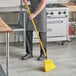 A person in an apron sweeping a floor with a yellow Lavex angled broom.