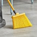 A person sweeping the floor with a yellow Lavex angled broom.