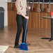 A woman sweeping the floor with a Lavex blue broom on a wooden floor.