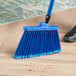 A person sweeping a wood floor with a blue Lavex broom with a metal handle.