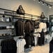 A black UDIZINE wall-mount clothing display with faceouts and a hanging rail for shelves.