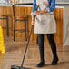 A woman using a Lavex black metal threaded broom handle to mop the floor.