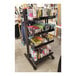 A black Udizine mobile retail clothing display stand with shelves holding various products.