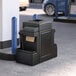 A black trash can with a brown bag inside sitting in front of a gas station.
