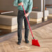 A man using a Lavex red angled broom to sweep the floor.