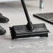A person using a Lavex black brush head with squeegee to clean a floor.