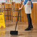 A woman using a Lavex black deck brush with squeegee to clean the floor.