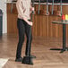 A woman using a Lavex angled black broom with a metal handle to sweep the floor.