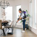 A woman using a ProTeam backpack vacuum cleaner to vacuum a dining room.