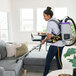 A woman wearing a ProTeam backpack vacuum cleaning a couch.