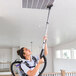 A woman wearing a ProTeam GoFit backpack vacuum cleaning a ceiling.