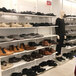 A mannequin in a white room stands in front of white Udizine retail clothing display shelves filled with black shoes.