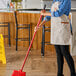 A woman in an apron holding a Lavex red metal broom handle.