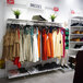 A white UDIZINE wall-mounted retail clothing display with faceouts and hanging rails for shelves.