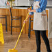 A woman in an apron sweeping a floor with a yellow Lavex metal broom handle.
