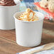 Two white Choice paper food cups filled with ice cream on a counter.