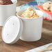 Two Choice white paper food cups filled with ice cream and topped with a vented paper lid.