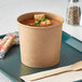 A Choice kraft paper food cup filled with soup on a tray.